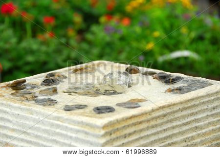 Fountain with bebbles in japanese garden with flowers in background