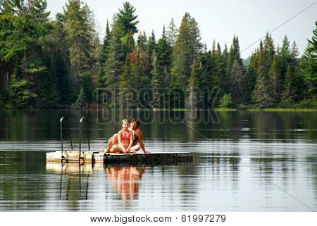 Grangmother and granddaughter sitting on a diving platform on a scenic lake