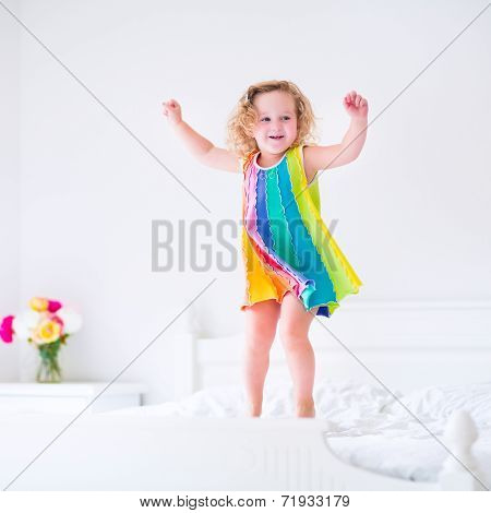 Cute little curly toddler girl jumping on a big white bed