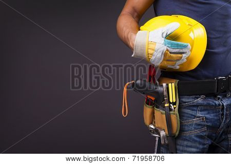 Close up of a worker with toolbelt and helmet against black background