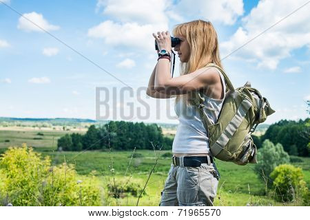 Hiker looking in binoculars enjoying spectacular view on the valley. Young woman using binoculars in