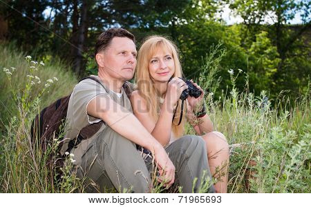 Young woman and man hiker with backpacks sitting by the forest enjoying view smiling happy. Young co