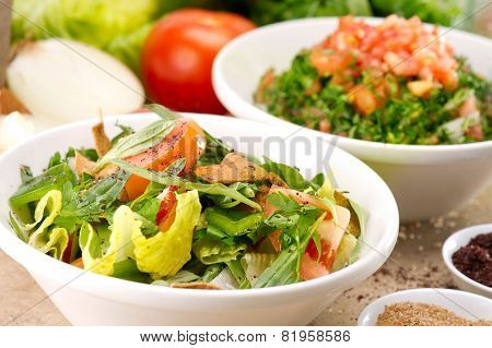 Plates of traditional Arabic salad fattouch and tabbouleh on a rustic background