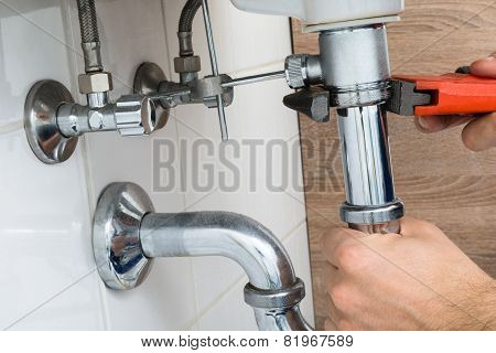 Male Plumber Fixing Sink In Bathroom