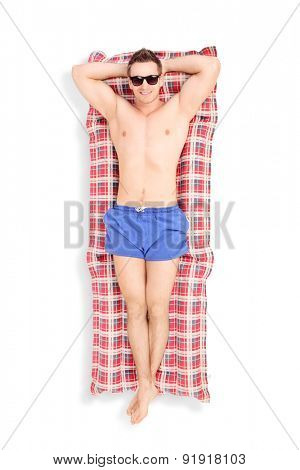 Full length portrait of a handsome young man with sunglasses sunbathing on a airbed isolated on white background