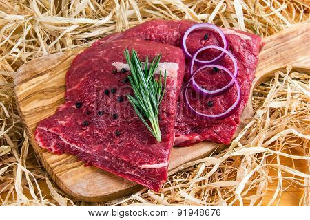 British Beef Flat Iron steak on cutting board and straw, rosemary and onion
