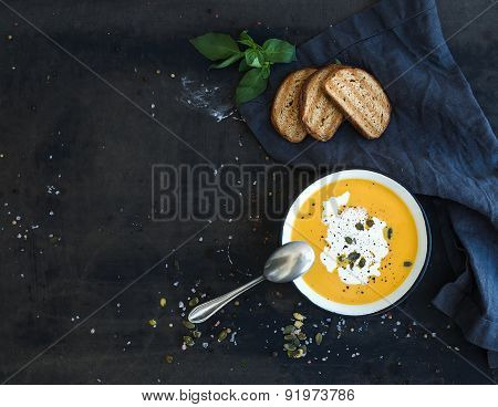 Pumpkin soup with cream, seeds, bread and fresh basil on grunge black background