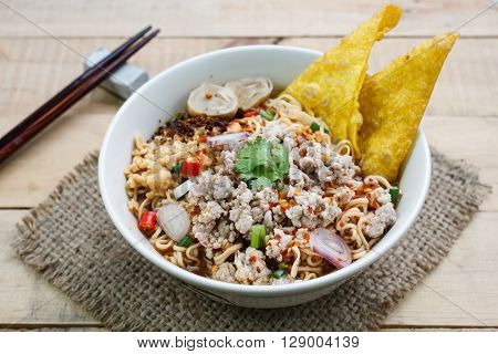 Spicy instant noodle soup with minced pork on wood background.