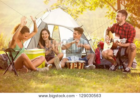Laughing group of young people enjoy in music of drums and guitar on camping trip