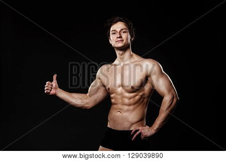 Muscular And Fit Young Bodybuilder Fitness Male Model Showing Thumb-up And Posing Over Black Backgro
