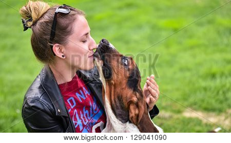 Young woman with an affectionate one year old Basset hound (Canis lupus familiaris) in the yard of a hobby farm.  Girl loves her dog, wet kisses from her one year old Basset hound.