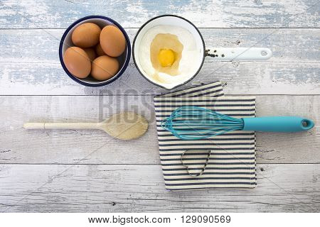 Eggs in a bowl with a whisk on a rustic wood table top shot from above