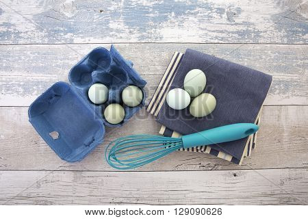 Eggs in a box with a whisk on a rustic wood table top shot from above