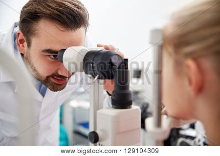 health care, medicine, people, eyesight and technology concept - optometrist with non contact tonometer checking patient intraocular pressure at eye clinic or optics store
