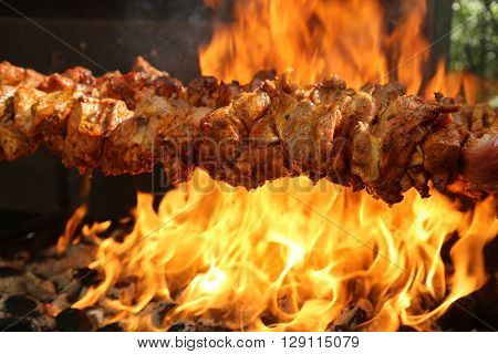 A spit roast on a grill with flames in the background