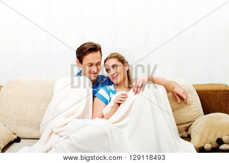 Smiling loving couple sitting on couch with blanket