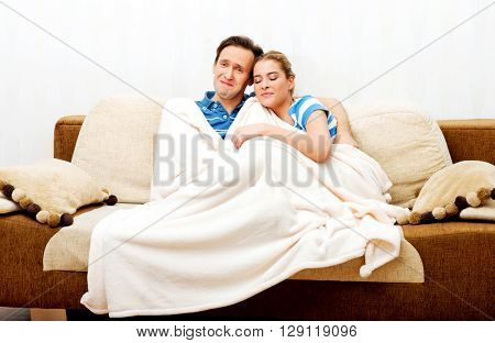 Smiling loving couple sitting on couch with blanket