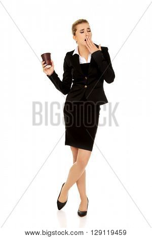 Tired yawning business woman holding a paper cup of coffee