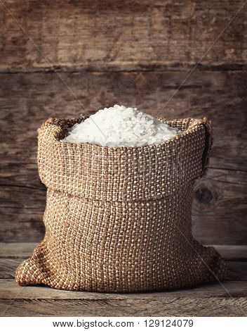 raw white rice in burlap sack on wooden background. Filling bag with rice. White rice on wooden background. Grains of rice in bag