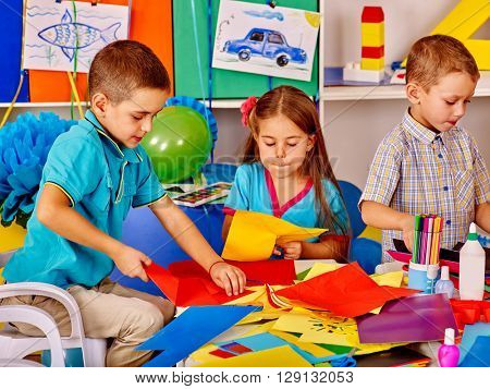 Group children holding colored paper on table in kindergarten . Children together work with paper in art class.