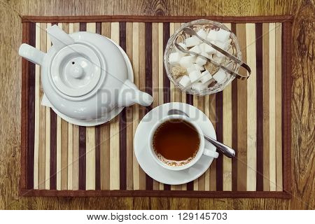 Top view of a cup of tea teapot and sugar bowl on a wooden background