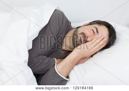 man with beard lying in a bed with white bedding