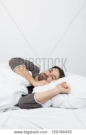 man with beard lying in a bed with white bedding