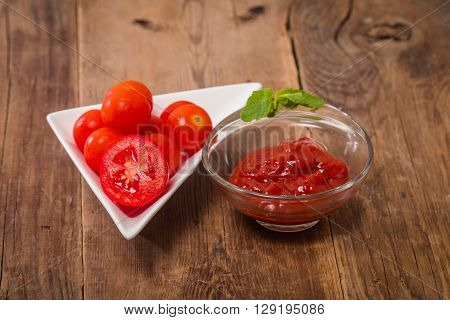 Tomato sauce, gaspacho, ketchup in glass bowl with tomatoes on wooden background