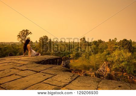 ANGKOR WAT CAMBODIA - JANUARY 28 2015: Young beautiful woman watching sunset at the top of Phnom Bakheng at Angkor Cambodia