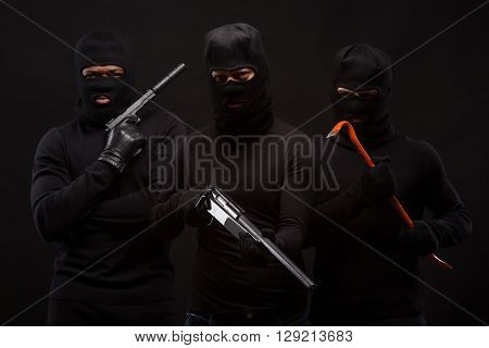 Murders in masks with machine-guns and crowbars over black background. People ae going to atack someone special. Isolated on black.