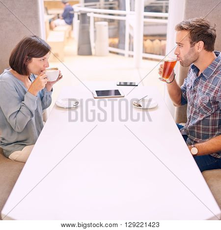 Couple looking at each other as they take their first sip on their first date after meeting online through a dating agency. There is a phone and tablet on the table.