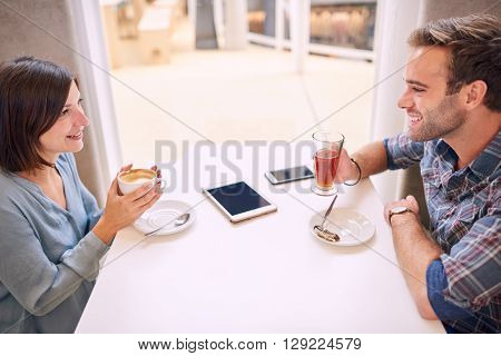 Old friends laughing and happy while they look at each other sitting in a beautiful light coffee shop with a smartphone and a tablet lying on the table infront of them.