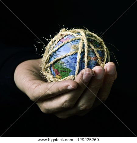 closeup of a young man with a world globe in his hand tied with rope, with a dramatic effect