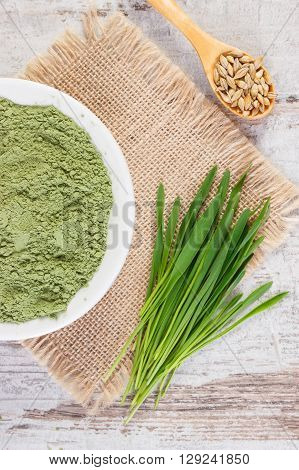 Young powder barley in bowl barley grass and grain on jute canvas old wooden background healthy nutrition and lifestyle body detox