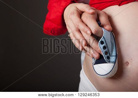 Young pregnant couple is holding baby shoes