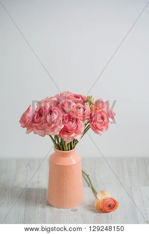 bunch of pale pink ranunculus persian buttercup light background, wooden surface. glass vase.  spring, summer