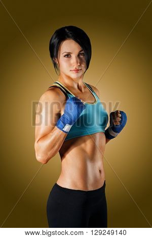 Young cute woman shows good fitness shape. Sporty strong body, girl in fitness wear shows biceps muscle. Slim brunette at yellow background, studio portrait. Female body building. Fitness trainer.