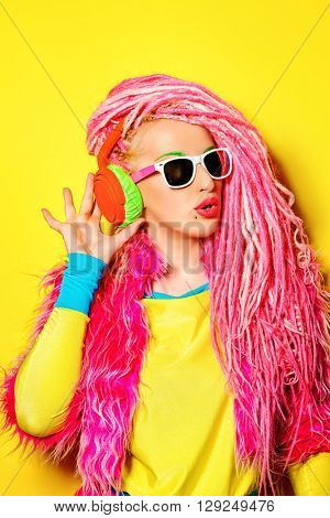 Glamorous modern DJ girl wearing bright clothes, headphones and bright dreadlocks. Disco, party. Bright fashion.