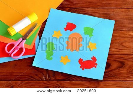 Sea animal and fish DIY Crafts Project Ideas for Kids. Children's paper crafts. Sheets of colored paper, scissors, glue on wooden background. Card with paper marine inhabitants