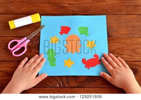 Card with sea animals and fish. Kids crafts idea project. Glue, scissors. Child put his hands on a table