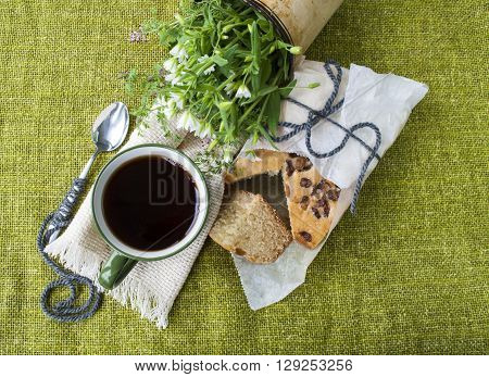 cup of black tea with cake on background of green textiles