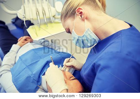 people, medicine, stomatology and health care concept - female dentist in mask with dental mirror and probe checking male patient teeth up at dental clinic office