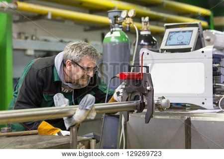Industrial operator setting  computer controlled process of orbital welding machine in  stainless steel pipes manufacturing workshop.