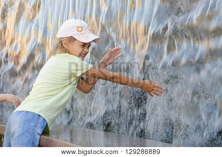 Cheerful Six Year Old Girl In Summer Clothes Hand Trying To Get The Water Artificial Waterfall