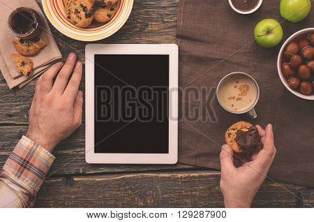 Man communicate via the Internet using the tablet while sitting at a wooden table in the morning. Male eating breakfast and communicating via the Internet using the tablet