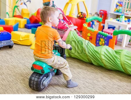 boy sitting on a toy motorcycle. child playing in a room with a lot of scattered toys