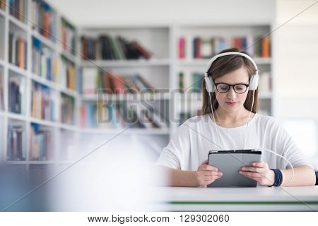 female student study in library using tablet and searching internet while  Listening music and lessons on white headphones