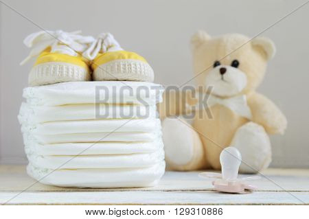 Some nappies on a white wooden table. Sneakers, a pacifier and a teddy bear. Empty copy space for editor's text.
