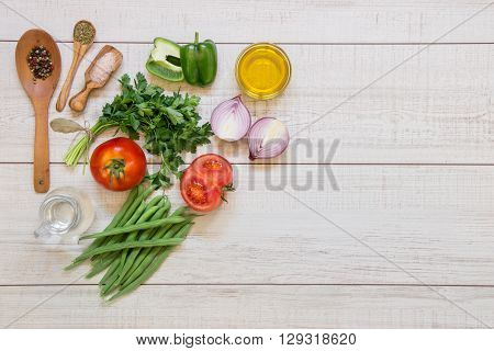 Left fresh vegetables ready to cook tomatoes peppers green beans onions parsley spices in wooden spoons on light wood background right empty space. Horizontal.Top view.
