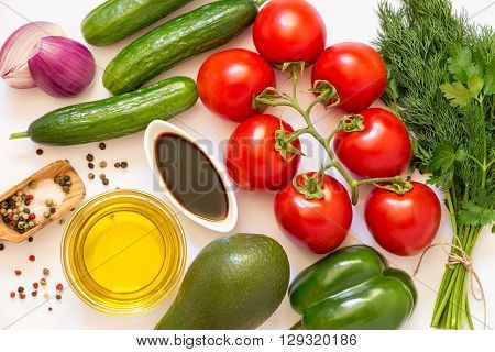 Vegetables ready to cook: tomatoes cucumbers pepper avocado onion parsley dill and olive oil balsamic salt pepper on white background. Horizontal. Top view.